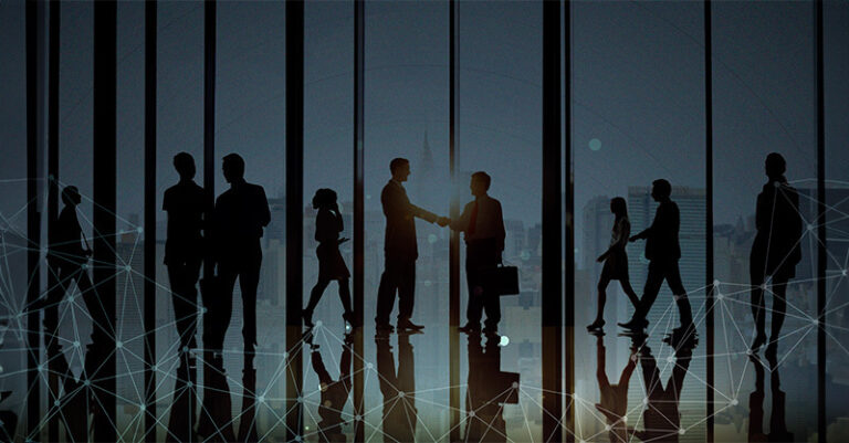A silhouette of two people shaking hands with more people walking in a room with windows.